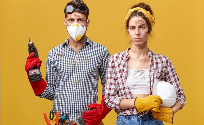 Serious couple doing repair at home standing against yellow background.