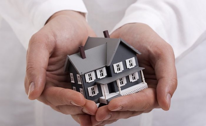 Man in white holding a model of a house in his hands.