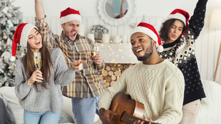 Happy New year. Multiethnic company dancing with champagne, black man playing Christmas song on acoustic guitar, copy space