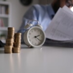 Businessman writing notes in documents model on stack of coins, in business, saving money