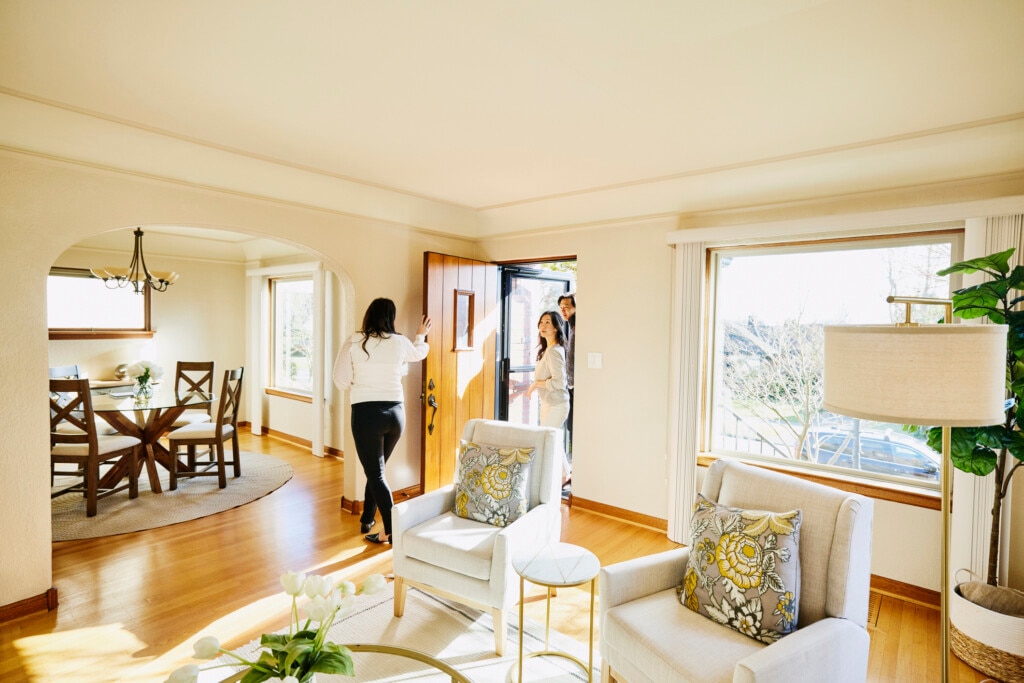 Wide shot of couple walking through front door of home for sale with real estate agent during open house